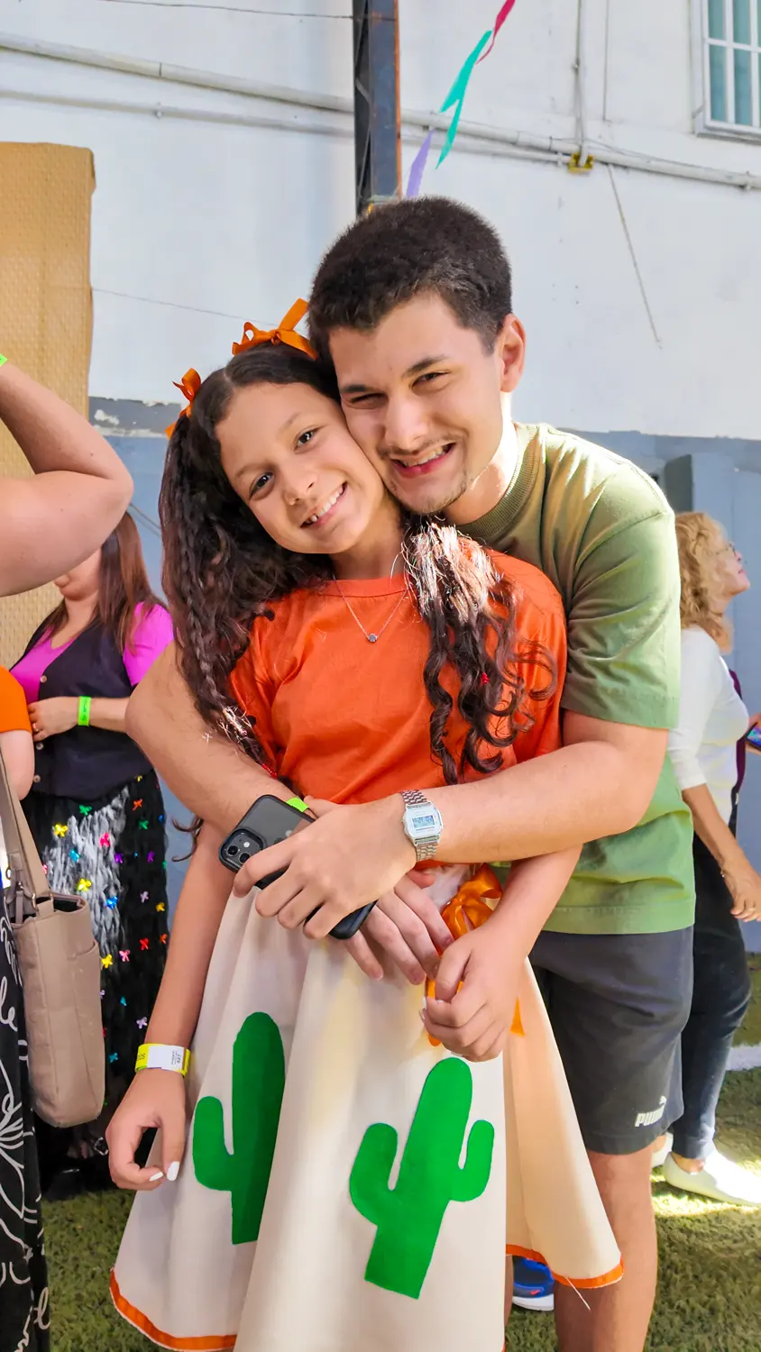 Aluna fantasiada para a festa junina, sorrindo abraçada a um familiar
