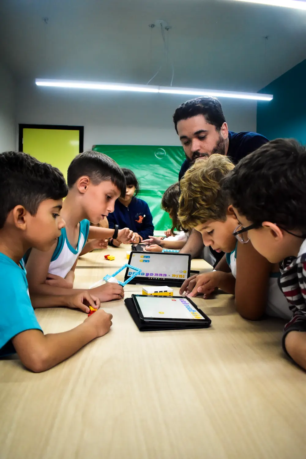 Alunos do Fundamental I da unidade Icaraí em volta da mesa, programando com tablets ao lado do professor