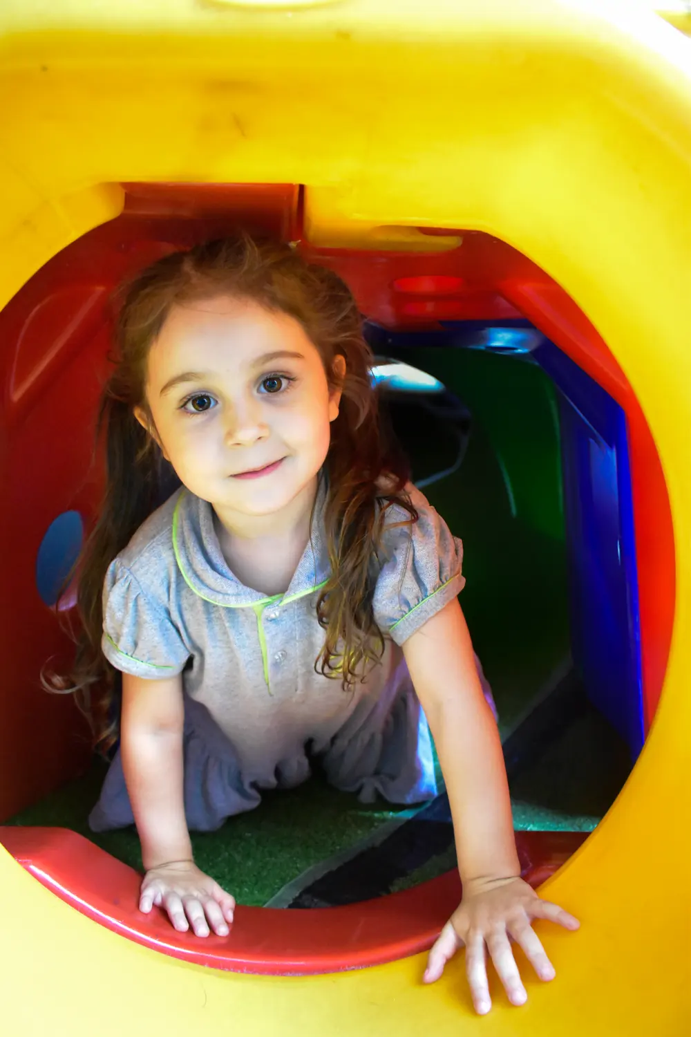 Aluna da Educação Infantil do ZH+ sorrindo dentro de um túnel colorido do parquinho