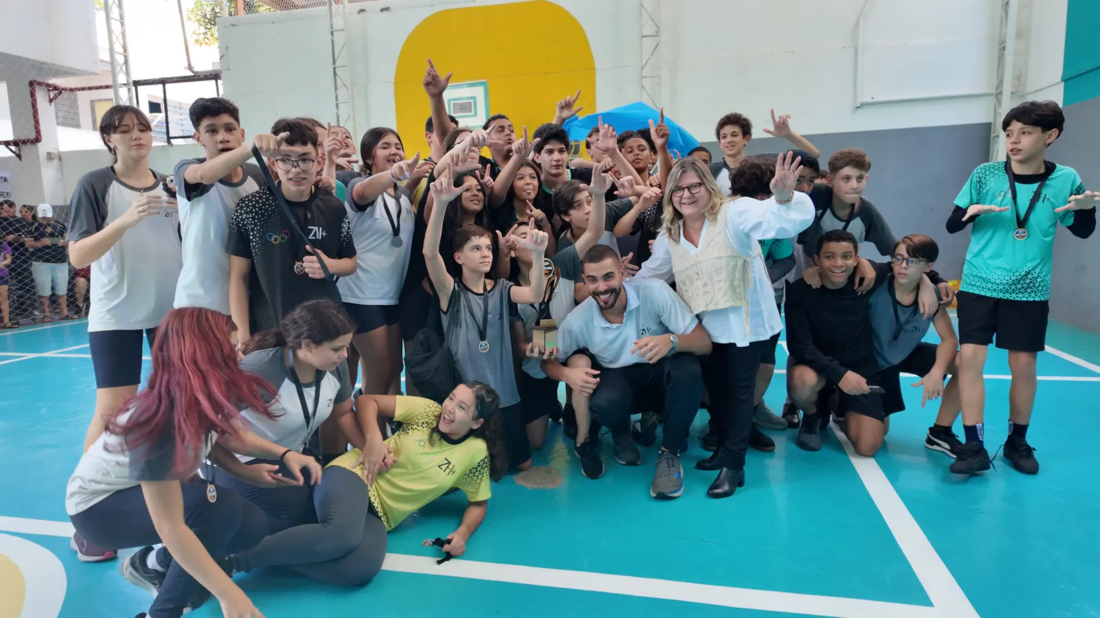 Alunos da unidade Vila Isabel comemorando na quadra, com medalhas no pescoço, ao lado da equipe