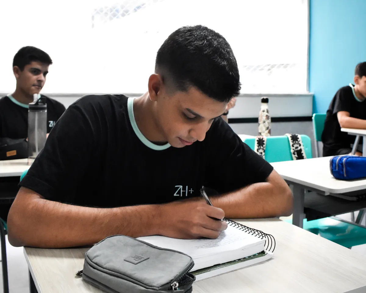 Aluno do Ensino Médio escrevendo no caderno durante a aula